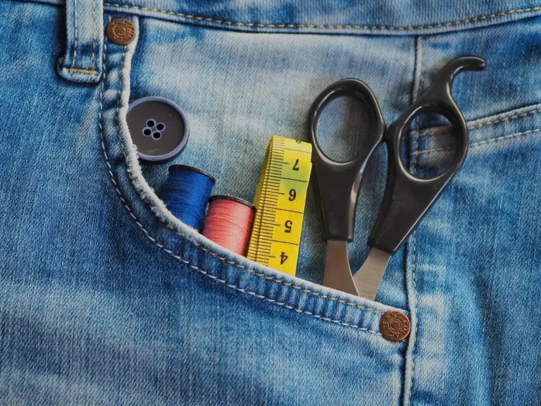 Poche de jean bleu en gros plan avec dans la poche du matériel pour coudre ou réparer: bouton, fil, metre, ciseau